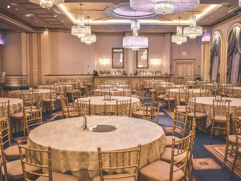 A hotel ballroom set with round tables under chandeliers