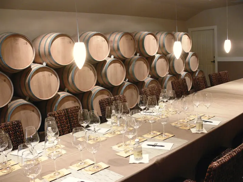 A winery barrel room with a long tasting table set with glasses